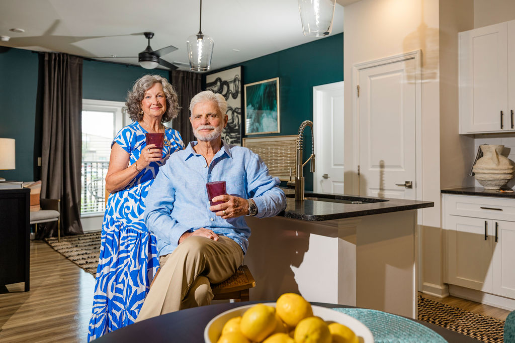 Retired couple poses at countertop in upscale kitchen apartment at Evolve Waterford in Belville, NC.